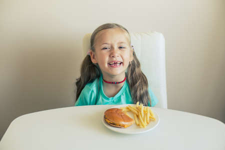 Smiling Little girl seats by the table with hamburger and French fries dishの写真素材