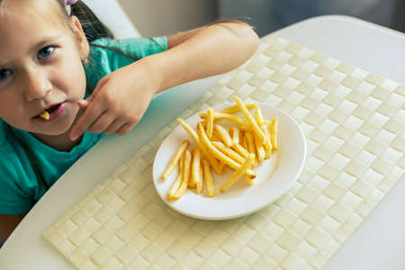 Close-up of a little girl eating French fries at the kitchenの写真素材