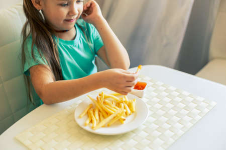 Close-up of a little girl eating French fries at the kitchenの写真素材