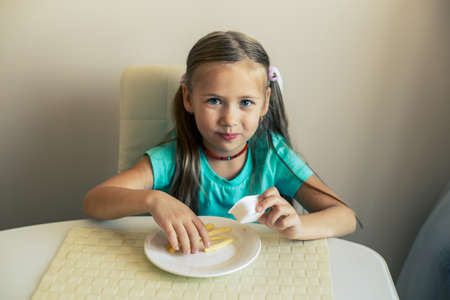 Close-up of a little girl eating French fries at the kitchenの写真素材