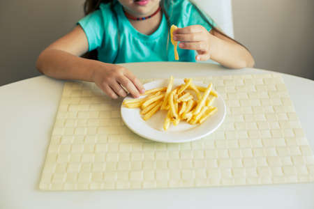 Close-up of a little girl eating French fries at the kitchenの写真素材