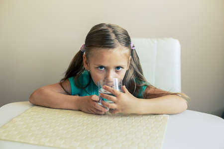 Beautiful little girl drinks clean water from a transparent glass.の写真素材