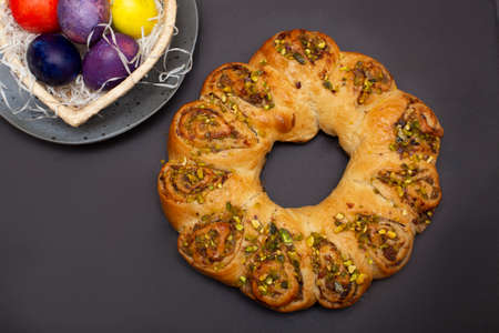 Easter roll with nuts and colored eggs in heart shaped basket. Brown background..の写真素材