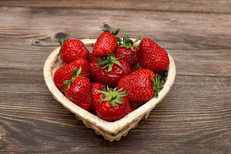 Ripe strawberries in a heart-shaped basket on a wooden tableの写真素材