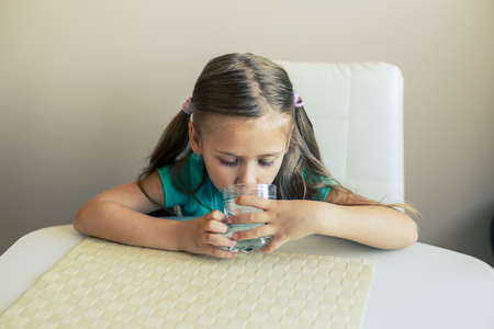 Beautiful little girl drinks clean water from a transparent glass.の写真素材