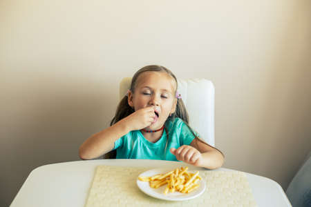 Close-up of a little girl eating French fries at the kitchenの写真素材