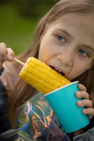 Beautiful blue-eyed girl eating boiled corn in the park.