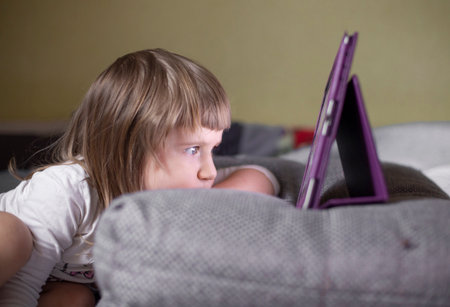 The child looks at the tablet, which is on the pillowの写真素材