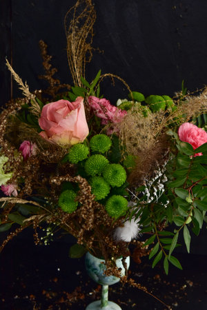 Floristry, a beautiful ornate natural feminine bouquet of roses, carnations, grasses and green twigs on a black background.の写真素材