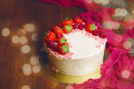 Christmas cake with strowsberry raspberry chocolate and lights bokeh homemade bakery on wooden backgroundの写真素材