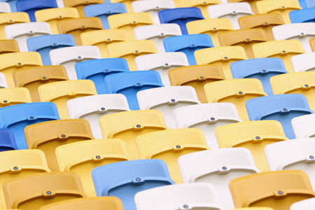 A field of yellow, white and blue empty plastic seats on the stadiumの写真素材
