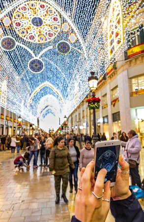 MALAGA, SPAIN - DECEMBER 9,2017: Woman takes a photo of Christmas decorations on Calle Marques de Larios street in the centre of Malaga city, Andalusia, Spain. Most popular pedestrian street of Malagaのeditorial素材