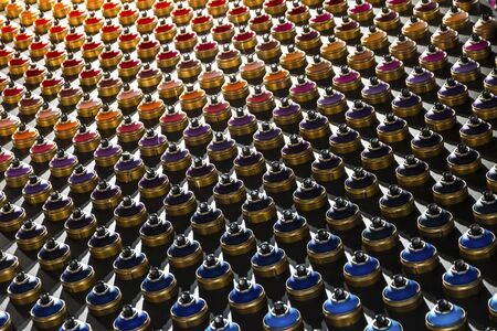 Rows of color paint spray cans placed on a black wall.