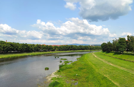 Scenic summer view of Uzhhorod city and Uzh river, Transcarpathia, Ukraine. A serene river winding through green fields under a partly cloudy skyの写真素材