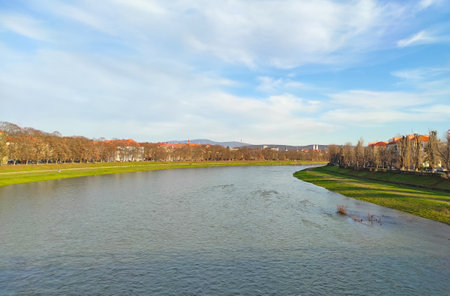 Picturesque autumn view of Uzhhorod city and Uzh river, Transcarpathia, Ukraine. Serene riverside landscape captures the gentle flow of water under a cloudy sky alongside a grassy bankの写真素材