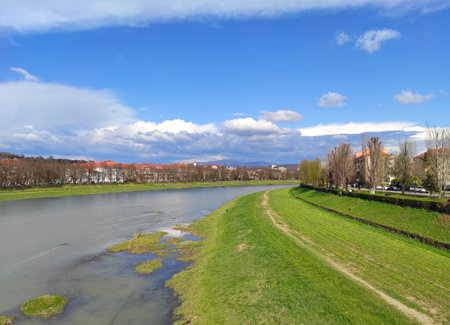 Scenic spring view of Uzhhorod city and Uzh river, Transcarpathia, Ukraine. Scenic view of a calm river with lush banks under a bright blue sky with scattered clouds in early springの写真素材