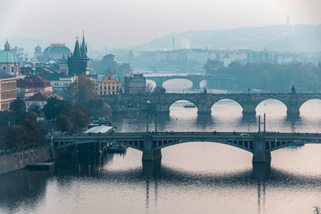 Panoramic view of Prague bridges over the Vltava river, Czechia. Calm, misty morning over Prague showing multiple arched bridges crossing the Vltava, with historic rooftops and domes lining the riverbankの写真素材