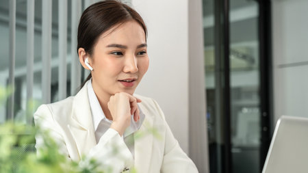 Asian businesswoman uses a laptop to analyze a company's financial business graph, Using a laptop for telecommunication work, Happy woman working in front of laptop screen, Modern private office room.の写真素材
