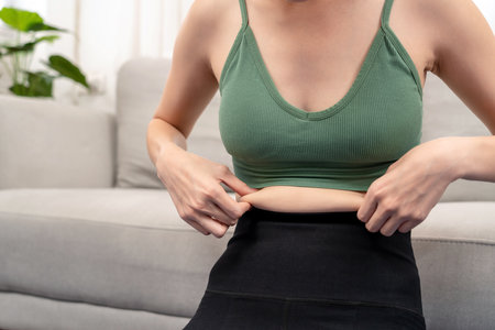 Sporty woman in sportswear hold cellulite on her belly waist and feeling bad with overweight while exercise in living room at home.の写真素材