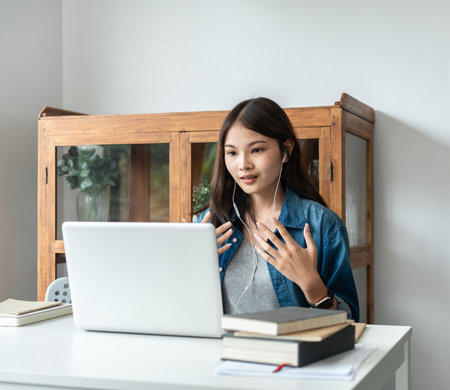 Young woman student in headset is video conference on laptop with classmates and lecturer after finished class in college.の写真素材