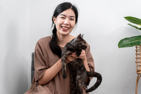 Beautiful woman is playing with a lovely cat to stroking and hugging while sitting to relaxation on carpet in the living room.の写真素材