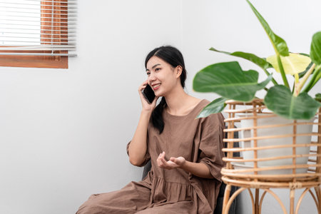 Beautiful woman is using smartphone to talking with friends while sitting to relaxation on carpet in the living room.の写真素材