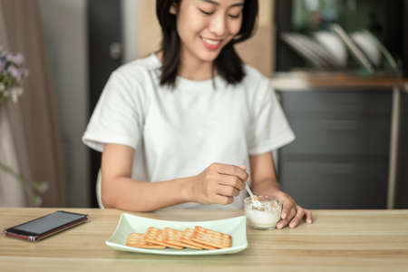 Tanned Asian woman eating yogurt and crackers for breakfast, Health care by eating a diet that is low in fat and calories, The most popular food of the working age, Wake-up activities.の写真素材