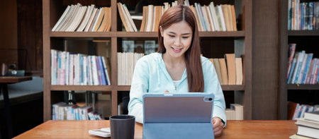 Female student is using tablet to do homework with classmates while reading data in the library.