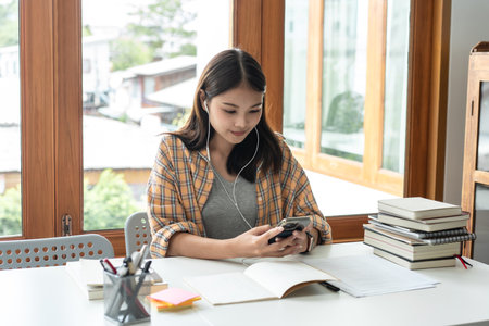 Young woman student in headset is video conference and chatting on smartphone with classmates and lecturer after finished class in college.の写真素材