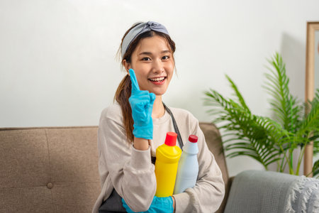 Housekeeper is wearing protective gloves to holding cleanser bottle and smiling to showing happy thumbs up gesture after successfully working to perform routine house cleaning.の写真素材