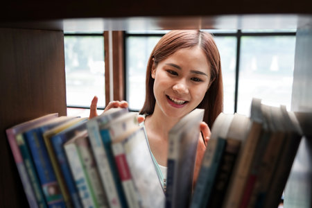Female student is standing in front of the bookshelf to choosing textbook or literature in library between take a break from studying lessons class at university.の写真素材