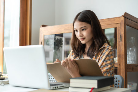 Young woman student is taking notes on notebook during learning lessons online on laptop with lecturer to preparing for examination in college.の写真素材