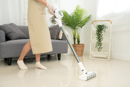 Housekeeper is using vacuum cleaner for cleanups and vacuuming dirt in living room while working to perform routine house cleaning.の写真素材