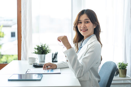 Businesswoman in suit is reading business data to thinking and analysis about strategy and planning of new business while holding glasses to smiling at camera and working on tablet in modern office.の写真素材