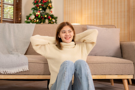 Young asian woman wearing sweater and put hands crossed behind head while sitting to relaxation in holiday on the floor in cozy living room of christmas decoration at home.の写真素材