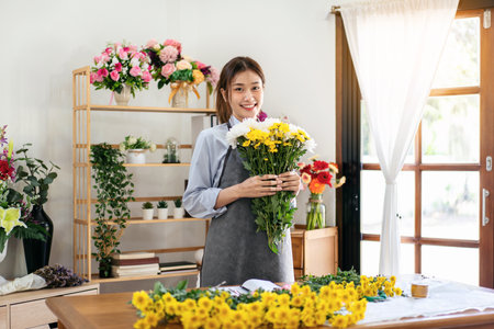 Female florist in apron smiling and holding chrysanthemum with enjoying while creating and designing floral for arrangement flower bouquet in her flower shop.の写真素材