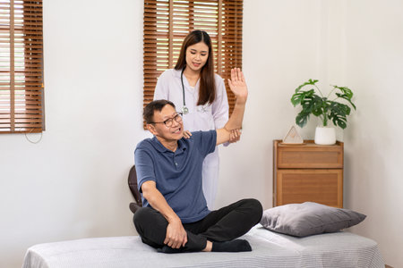Female physical therapist working and doing arm rehabilitation therapy for elderly patient sitting on hospital bed and talking to giving advice on treatment to patient.の写真素材
