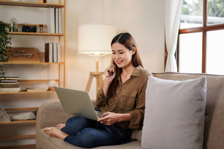 Female entrepreneur touching play her hair while sitting on big comfortable sofa to reading new business project and working on laptop in living room at home office.の写真素材