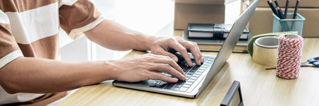 Male entrepreneur is using laptop to checking and taking receive online orders for prepare packing...