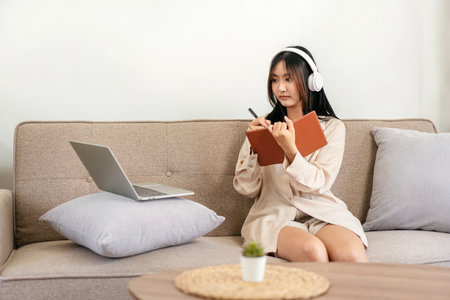 Female entrepreneur is sitting on big comfortable sofa and putting laptop on pillow while wearing...
