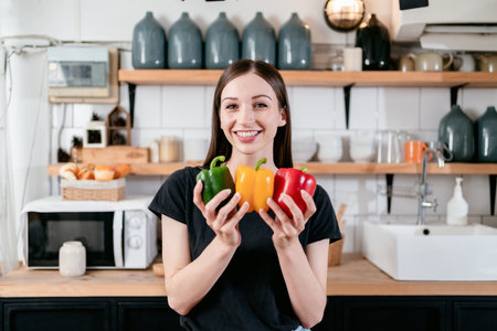 Woman holding colorful bell pepper in her hands with enjoying while preparing fresh vegetable and fruits with organic products on the table to cooking for healthy meal in modern kitchen at home.の写真素材