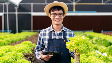 Man smart farmer holding tablet working and checking organic hydroponic vegetable quality in greenhouse plantation to preparing harvest export to sell.の写真素材