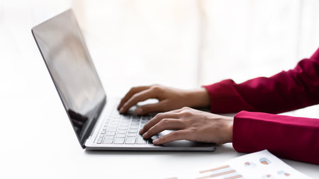 Businesswoman in suit thoughtful about accounting of new business and typing information with keyboard on laptop while working on the table in modern workspace.の写真素材