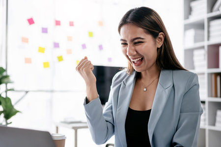 Accounting business concept, Accountant woman reads good news on laptop with excited and raising fist to celebrate achievement while working about investment with business planning finance.の写真素材
