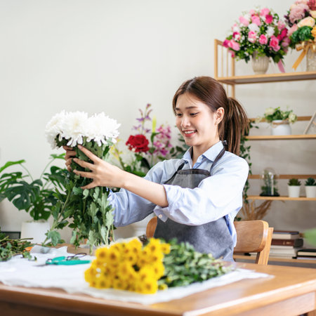 Female florist in apron holding white chrysanthemum to creating and designing floral for arrangement flower bouquet on the table in her flower shop.の写真素材