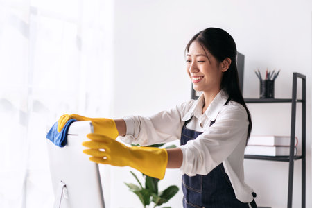 Housewife in apron wearing gloves to using microfiber fabric to wiping cleanup computer and furniture while working and cleaning in the house.の写真素材