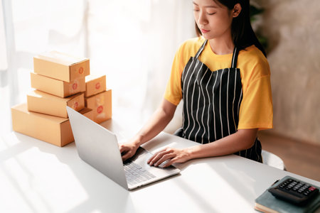 Small business parcel delivery concept, Female entrepreneur checking online order on laptop and packing product to shipment delivery for client while working about shopping online sales business.の写真素材
