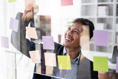 Business planning with share idea concept, Businessman working and writing information in notes on the glass wall and thinking to analysis about business planning in office.の写真素材