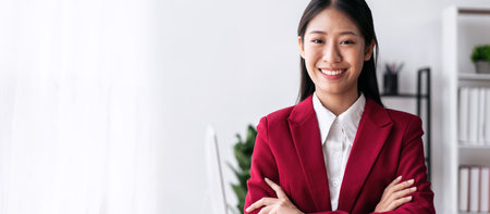 Confident businesswoman in suit smiling and standing with arms crossed while working about accounting of new business in modern workspace.の写真素材