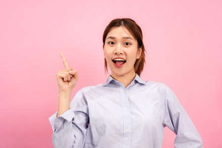 Young asian woman wearing long sleeve shirt and using hands with forefingers to pointing advertisement on copy space isolated over pink background.の写真素材